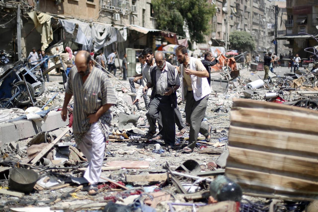 Drei Männer laufen über Schutt auf dem Marktplatz in Duma, Syrien Drei Männer laufen über Schutt auf dem Marktplatz in Duma, Syrien