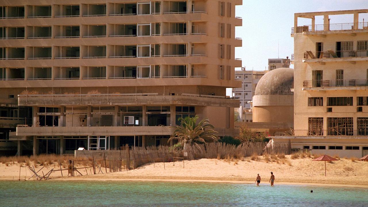 Zwei Touristen waten im Oktober 1998 in Strandnähe durch das flache Wasser. Sie nähern sich dabei der durch einen Stacheldrahtzaun markierten Demarkationslinie, die ihren Hotelkomplex (r) in Gazimagusa (ehemals Famagusta) von den leerstehenden Hotelruinen (l) der früheren Touristenstadt Varosha (Vorort von Famagusta) trennt.