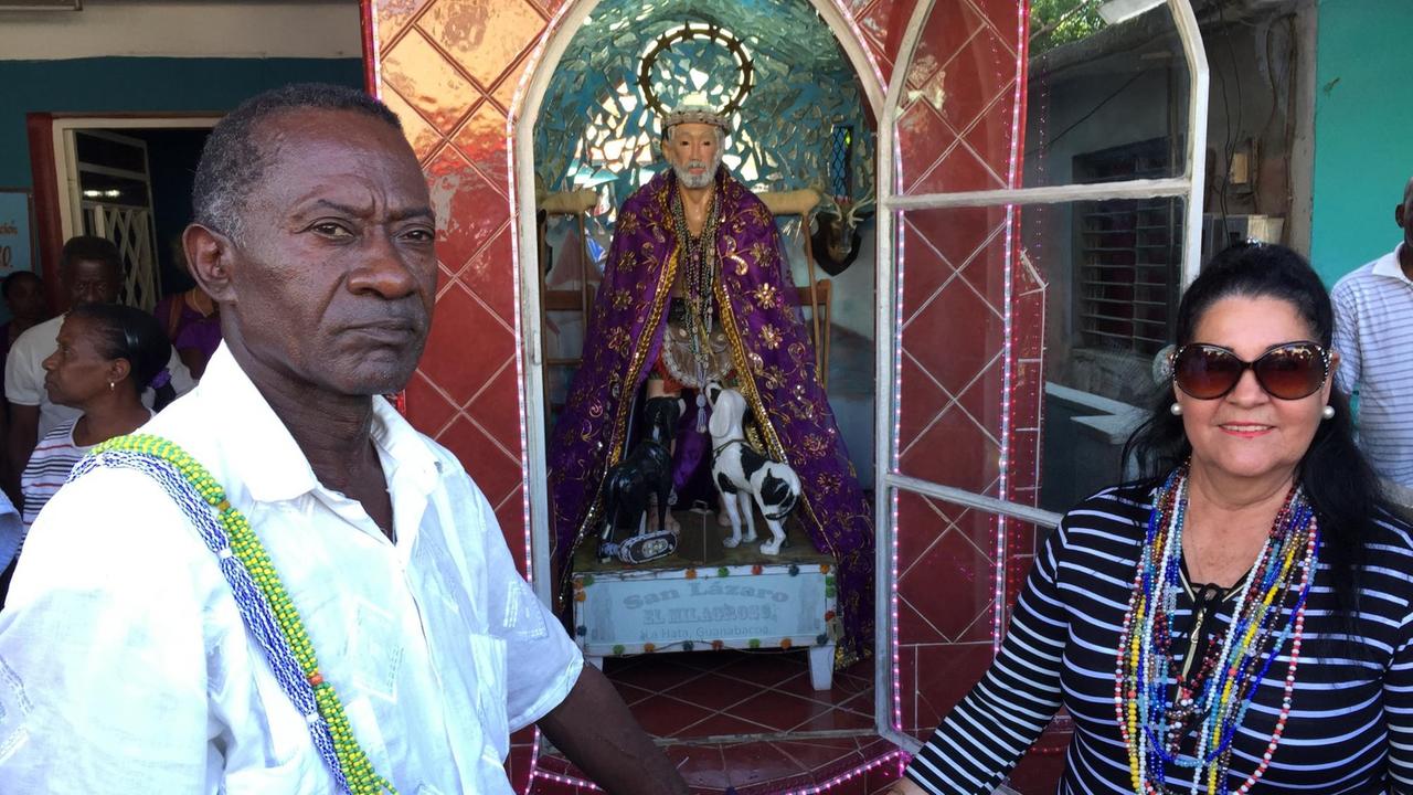 Der Babalao Andres Hernandez steht mit einer Frau vor der Statue des Heiligen Lazarus. Der Babalao Andres Hernandez steht mit einer Frau vor der Statue des Heiligen Lazarus.
