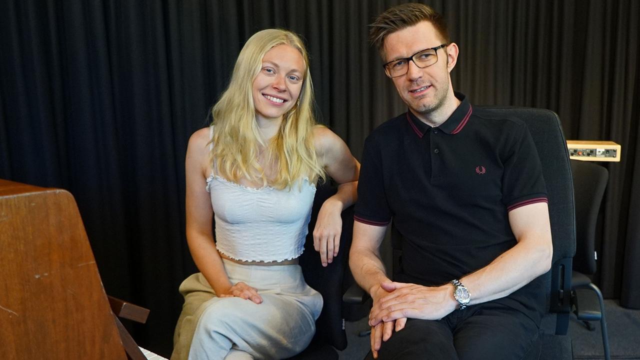 Die Sängerin und der Moderator sitzen nebeneinander und lachen in die Kamera. Die Sängerin und der Moderator sitzen nebeneinander und lachen in die Kamera.