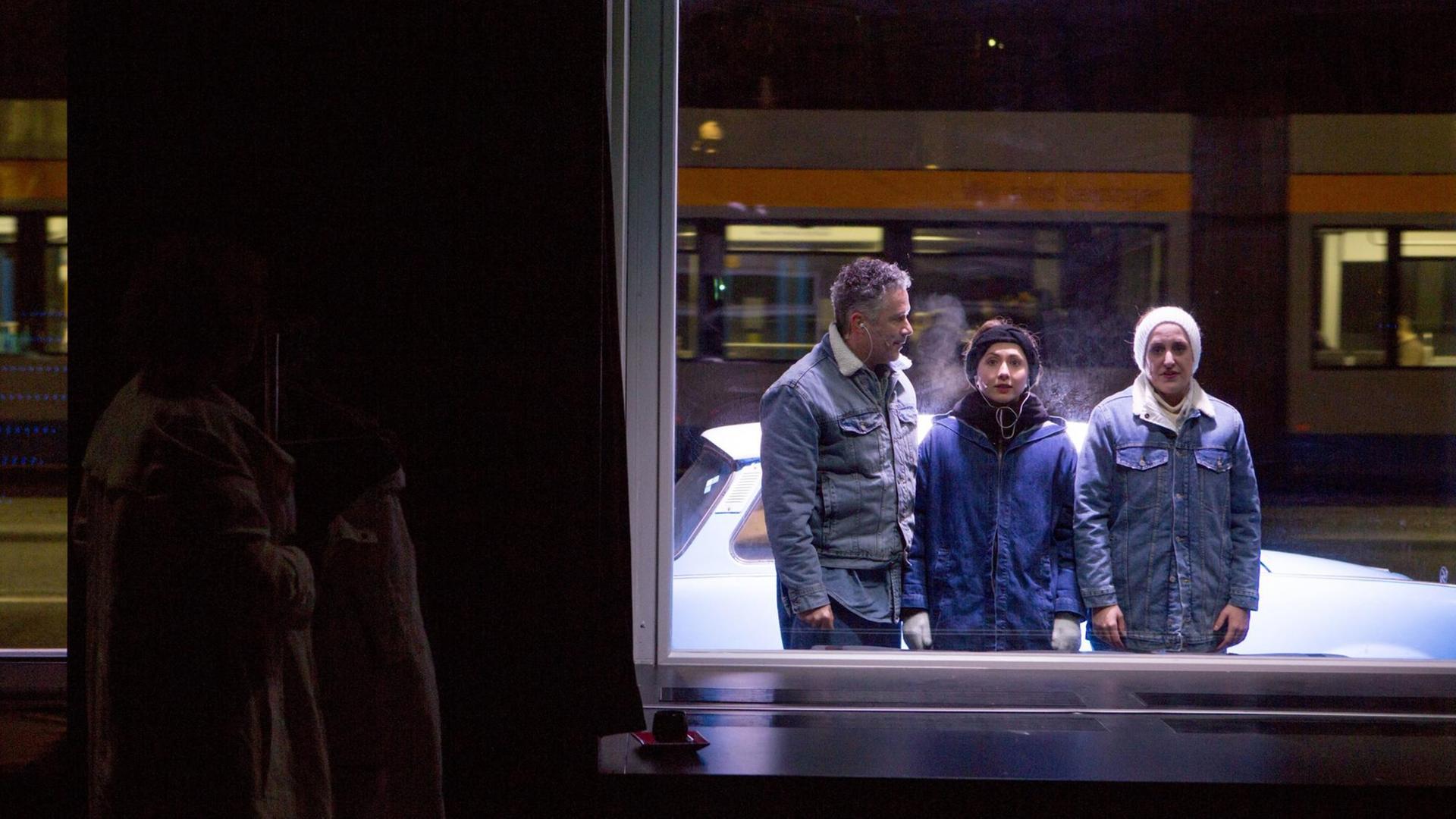 Drei Menschen stehen vor einem Schaufenster und schauen in den Raum hinein. Hinter dem Fester befindet sich ein Mensch im Dunkeln und schaut hinaus. Drei Menschen stehen vor einem Schaufenster und schauen in den Raum hinein. Hinter dem Fester befindet sich ein Mensch im Dunkeln und schaut hinaus.