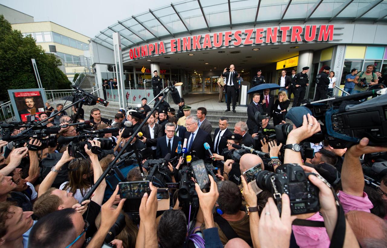 Bundesinnenminister Thomas de Maiziere (CDU, Mitte, l) und Bayerns Innenminister Joachim Herrmann (CSU, Mitte, r) geben einen Tag nach einer Schießerei mit Toten und Verletzten, vor dem Olympia-Einkaufszentrum (OEZ) in München (Bayern) ein Statement ab.