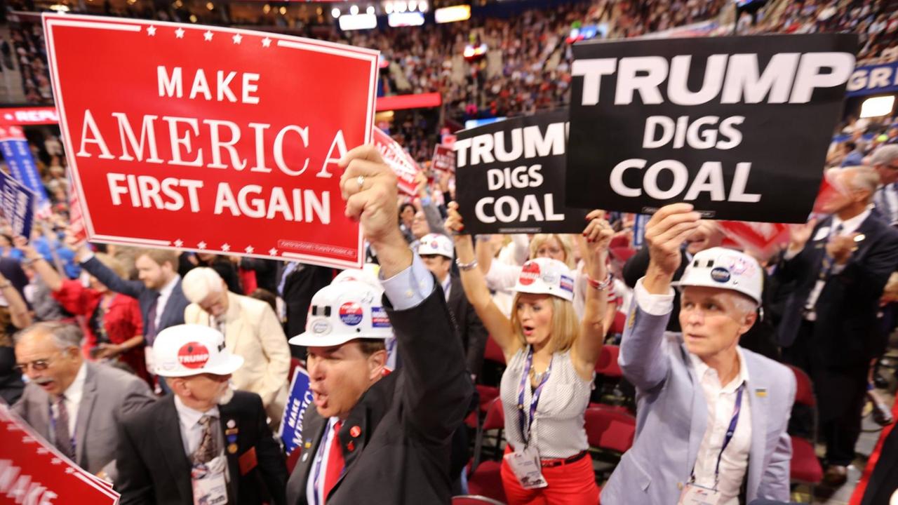 Sie sehen Frauen und Männer mit Helmen, einige halten Schilder hoch, auf einem steht "Trump gräbt nach Kohle". Sie sehen Frauen und Männer mit Helmen, einige halten Schilder hoch, auf einem steht "Trump gräbt nach Kohle".