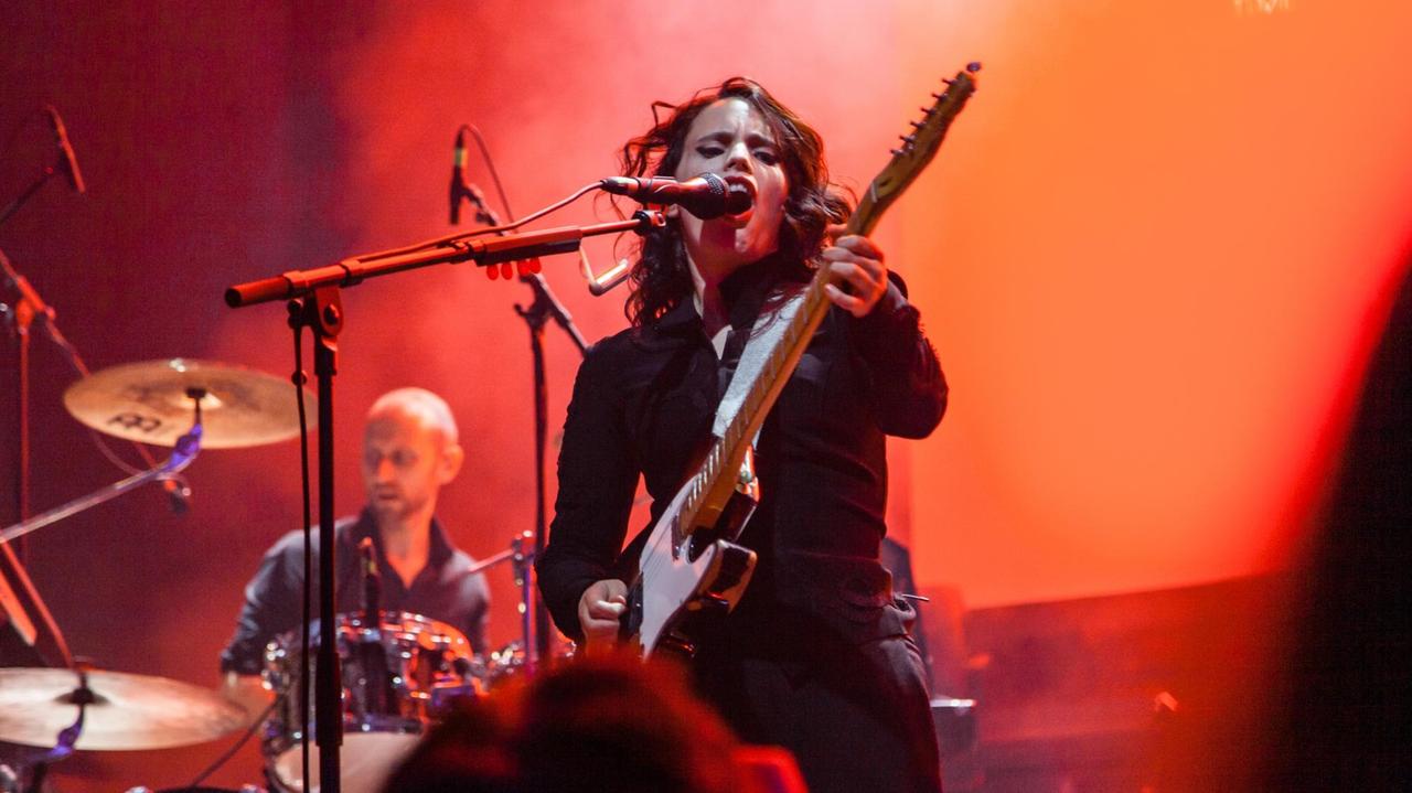 Auf einer grell rot erleuchteten Bühne steht die Sängerin mit ihrer Gitarre. Auf einer grell rot erleuchteten Bühne steht die Sängerin mit ihrer Gitarre.