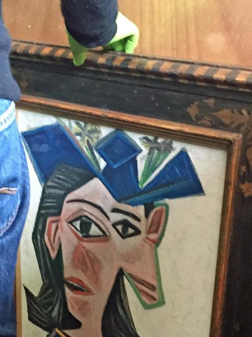Ein Mann mit Handschuhen transportiert das Gemälde "Buste de femme au chapeau" von Pablo Picasso.