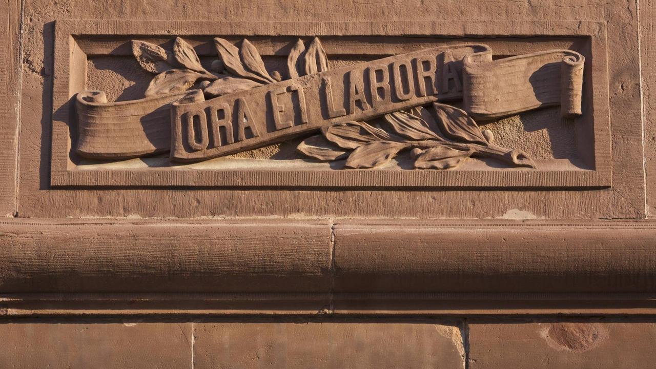 Geschwungenes Relief „Ora et labora“ an einer Hauswand Geschwungenes Relief „Ora et labora“ an einer Hauswand
