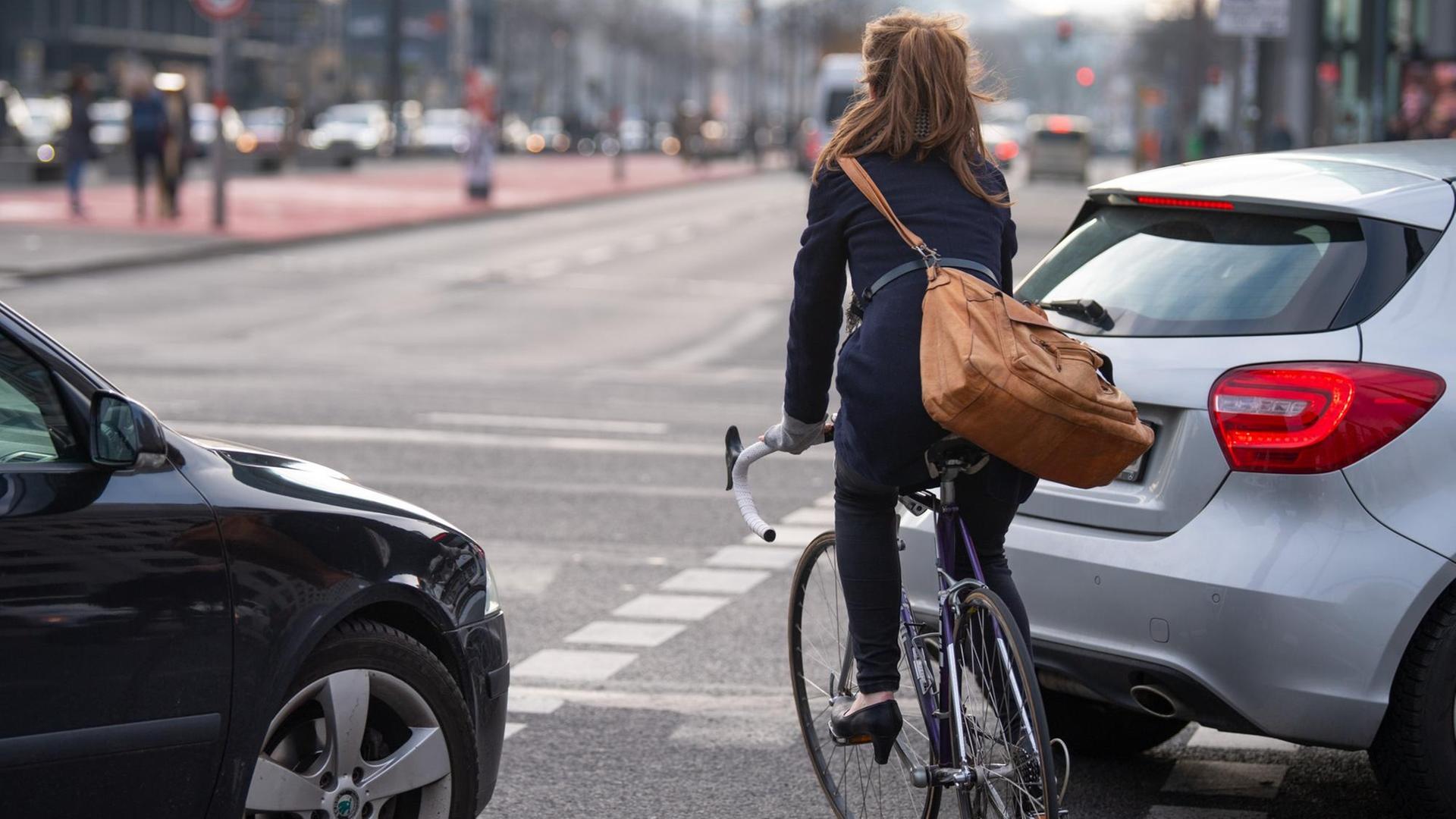 Ein Fahrradfahrerin fährt auf einem Fahrradweg auf einer Kreuzung zwischen zwei Autos entlang. Ein Fahrradfahrerin fährt auf einem Fahrradweg auf einer Kreuzung zwischen zwei Autos entlang.