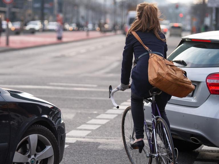 Ein Fahrradfahrerin fährt auf einem Fahrradweg auf einer Kreuzung zwischen zwei Autos entlang.