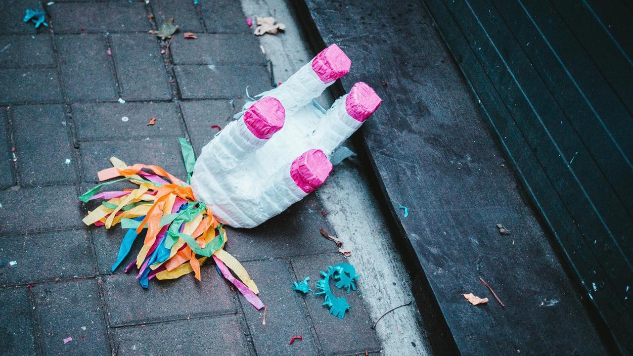 Eine Einhorn-Piñata liegt mit den Füßen nach oben auf dem Boden, drumherum liegen bunte Schnipsel. Eine Einhorn-Piñata liegt mit den Füßen nach oben auf dem Boden, drumherum liegen bunte Schnipsel.