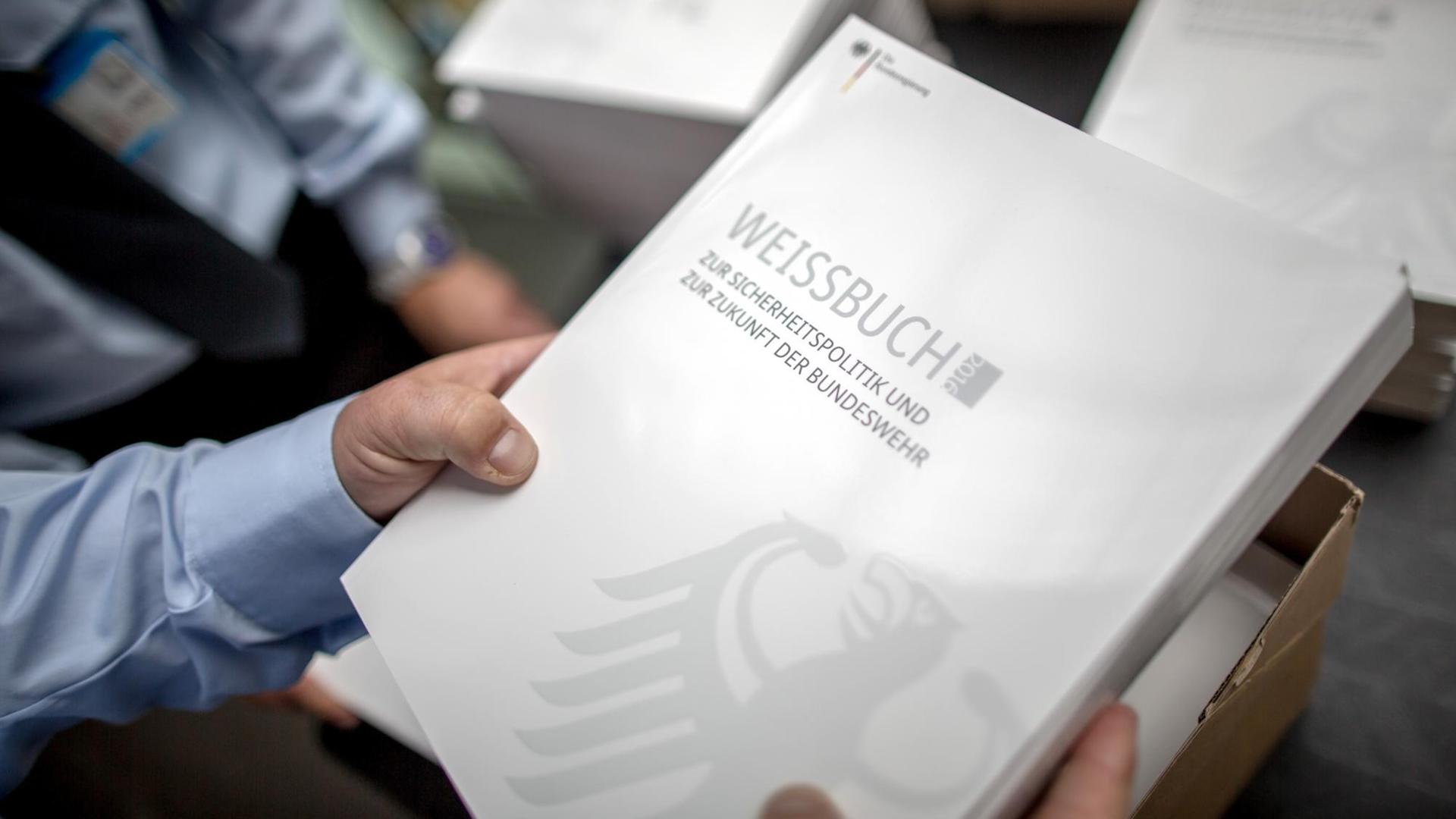 Eine Hand hält das neue Weißbuch zur Sicherheitspolitik. Eine Hand hält das neue Weißbuch zur Sicherheitspolitik.