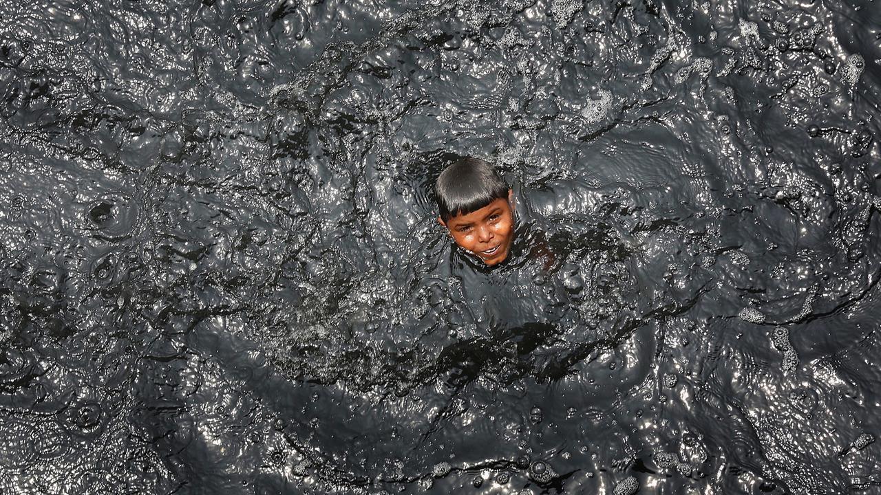 Ein Junge streckt seinen Kopf aus dem schwarzen Wasser des Flusses Yamuna in Neu Delhi. Ein Junge streckt seinen Kopf aus dem schwarzen Wasser des Flusses Yamuna in Neu Delhi.