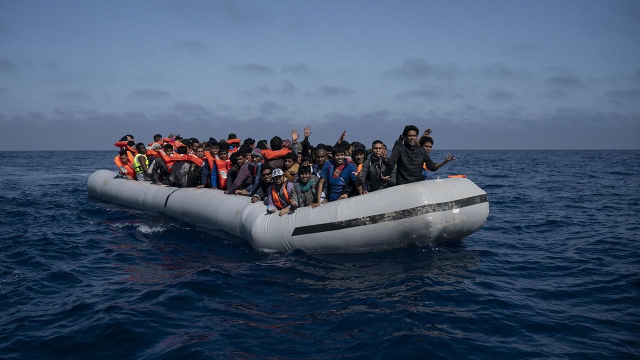 Bootsflüchtlinge mit orangefarbenen Rettungswesten in einem überfüllten Gummiboot vor der libyschen Küste. Bootsflüchtlinge mit orangefarbenen Rettungswesten in einem überfüllten Gummiboot vor der libyschen Küste.