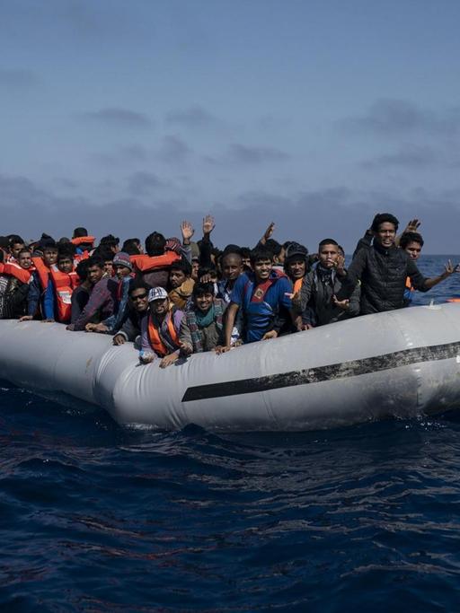 Bootsflüchtlinge mit orangefarbenen Rettungswesten in einem überfüllten Gummiboot vor der libyschen Küste.