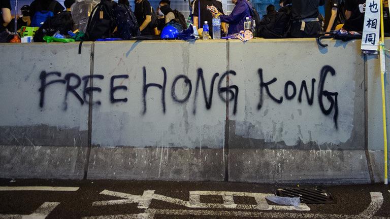 18.08.2019, China, Hongkong: Demonstranten sitzen am Abend auf einer Mauer, die mit einem Grafitti («Free Hong Kong») beschrieben wurde. In der ehemaligen britischen Kronkolonie Hongkong sind die Proteste gegen den Einfluss aus Peking in eine neue Runde gegangen. Die Demokratiebewegung hat zu einer weiteren Großdemonstration aufgerufen. Foto: Gregor Fischer/dpa | Verwendung weltweit 18.08.2019, China, Hongkong: Demonstranten sitzen am Abend auf einer Mauer, die mit einem Grafitti («Free Hong Kong») beschrieben wurde. In der ehemaligen britischen Kronkolonie Hongkong sind die Proteste gegen den Einfluss aus Peking in eine neue Runde gegangen. Die Demokratiebewegung hat zu einer weiteren Großdemonstration aufgerufen. Foto: Gregor Fischer/dpa | Verwendung weltweit