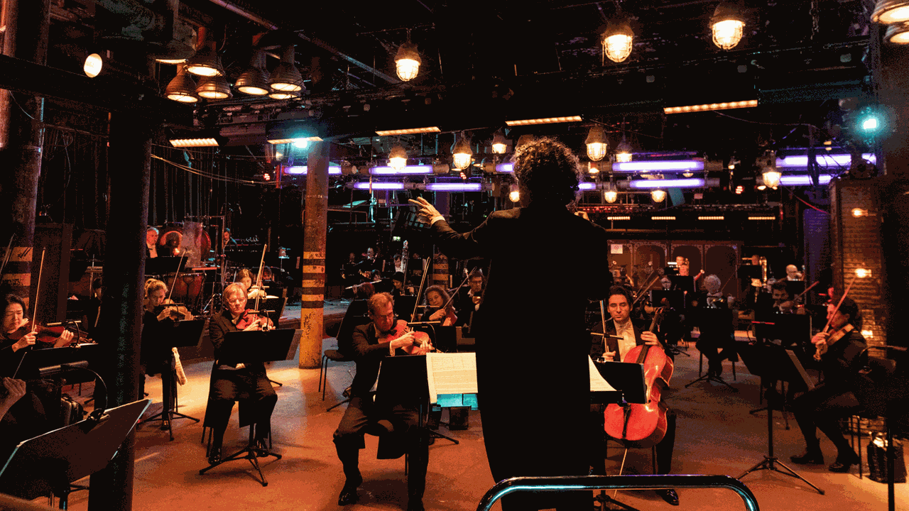 Das Orchester sitzt in einem niedrigen Clubraum mit Industriebeleuchtung.