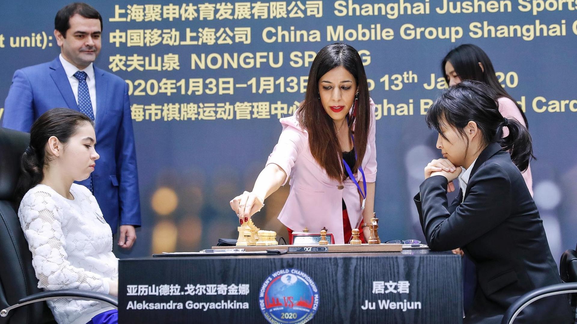 Die iranische Schiedsrichterin Shohreh Bayat bei der Schach-Weltmeisterschaft der Frauen in Schanghai. Bayat steht an einem Tisch, an dem zwei WM-Teilnehmerinnen vor einem Schachbrett sitzen, und greift nach einer Figur. Die iranische Schiedsrichterin Shohreh Bayat bei der Schach-Weltmeisterschaft der Frauen in Schanghai. Bayat steht an einem Tisch, an dem zwei WM-Teilnehmerinnen vor einem Schachbrett sitzen, und greift nach einer Figur.