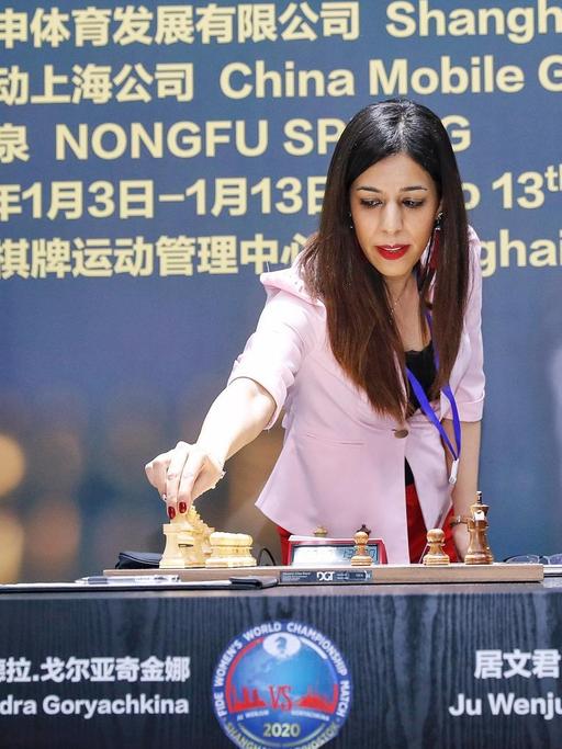 Die iranische Schiedsrichterin Shohreh Bayat bei der Schach-Weltmeisterschaft der Frauen in Schanghai. Bayat steht an einem Tisch, an dem zwei WM-Teilnehmerinnen vor einem Schachbrett sitzen, und greift nach einer Figur.