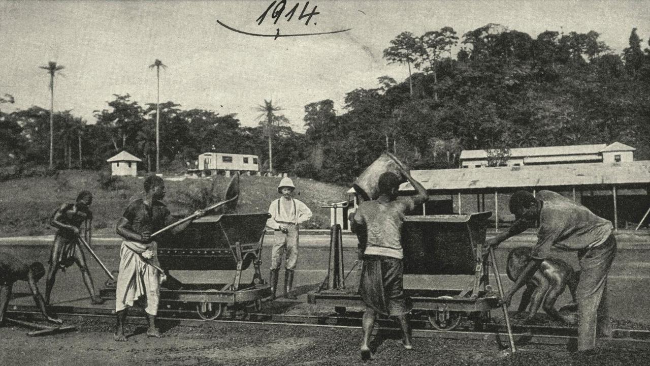 Unter Aufsicht eines deutschen Kolonisten verladen Arbeiter 1914 in Kamerun Kakaobohnen. Unter Aufsicht eines deutschen Kolonisten verladen Arbeiter 1914 in Kamerun Kakaobohnen.