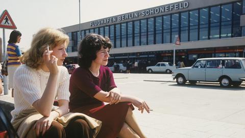 Zwei Frauen sitzen rauchend vor dem Flughafengebäude Berlin-Schönefeld.