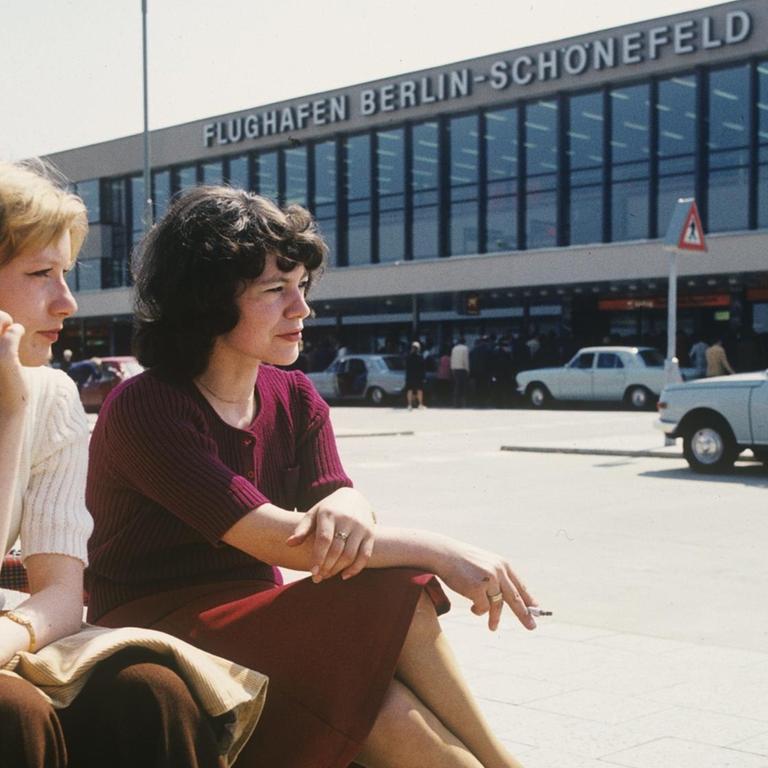 Zwei Frauen sitzen rauchend vor dem Flughafengebäude Berlin-Schönefeld.
