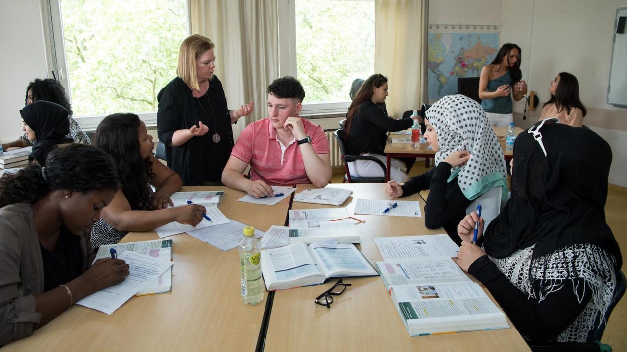 Unterrichtssequenz in der Berliner Berufsfachschule Paulo Freire: Schülerinnen und Schüler sitzen an Tischen und eine Lehrerin steht und spricht. Unterrichtssequenz in der Berliner Berufsfachschule Paulo Freire: Schülerinnen und Schüler sitzen an Tischen und eine Lehrerin steht und spricht.
