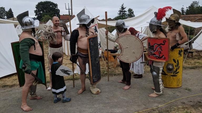 Sechs Personen sehen mit Schildern, Schwert, Helmen und Beinschienen aus wie Gladiatoren. Sechs Personen sehen mit Schildern, Schwert, Helmen und Beinschienen aus wie Gladiatoren.