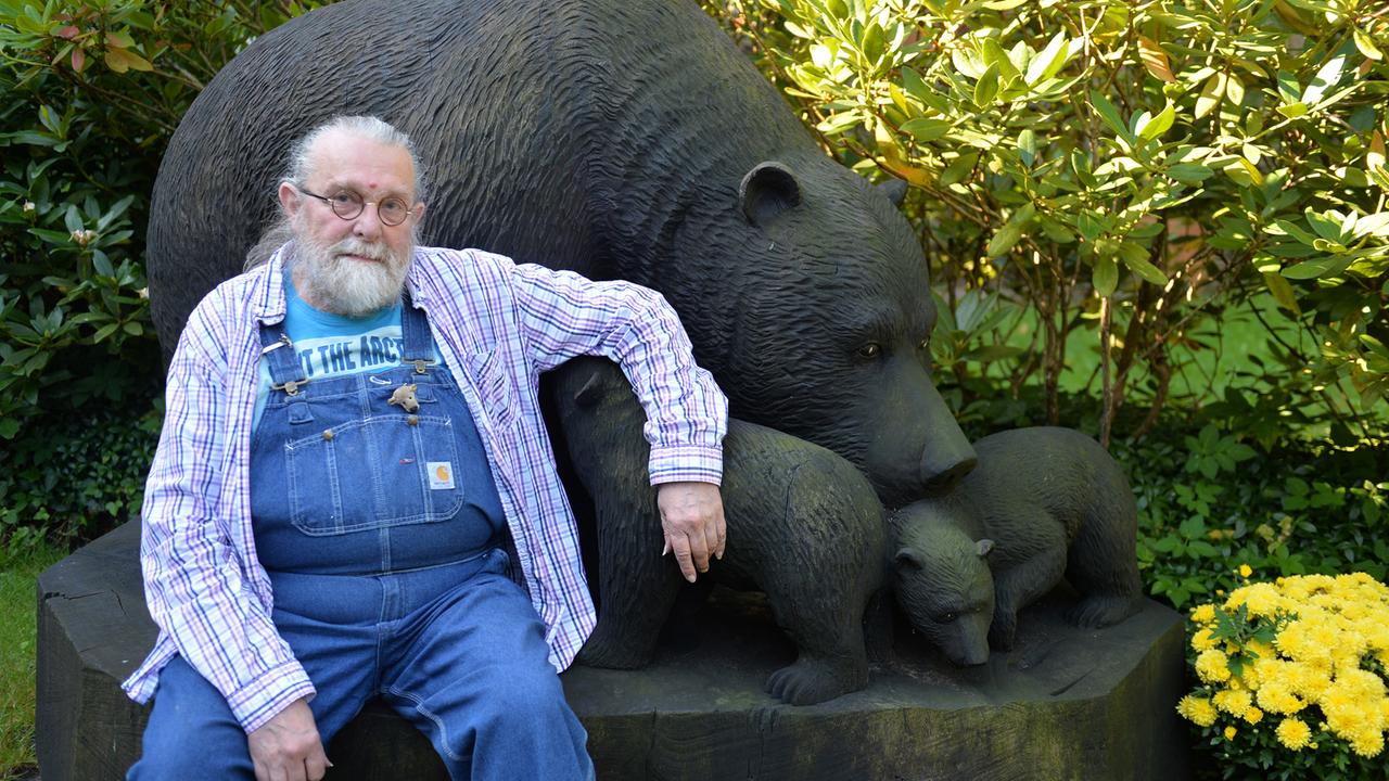 Richard Weize sitzt vor einer Bärenskulptur.
