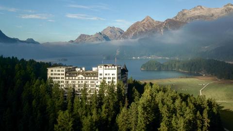 Zu sehen ist das Belle-Époque-Hotel Waldhaus Sils in einer atemberaubenden Umgebung, umrahmt von Bergen, einem See und Wäldern.