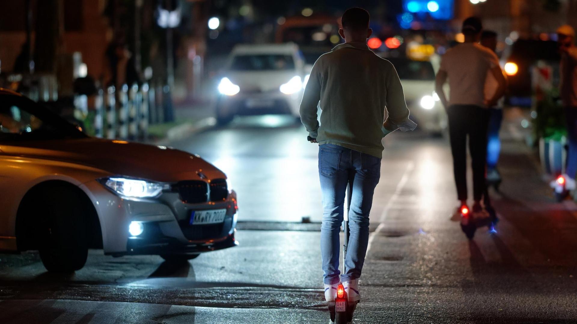 Menschen auf E-Scootern fahren in der Nacht durch eine Straße in der Düsseldorfer Altstadt. Auch Autos sind auf der Straße unterwegs. Menschen auf E-Scootern fahren in der Nacht durch eine Straße in der Düsseldorfer Altstadt. Auch Autos sind auf der Straße unterwegs.