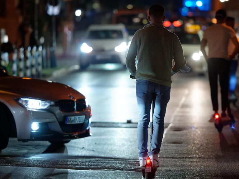 Menschen auf E-Scootern fahren in der Nacht durch eine Straße in der Düsseldorfer Altstadt. Auch Autos sind auf der Straße unterwegs.