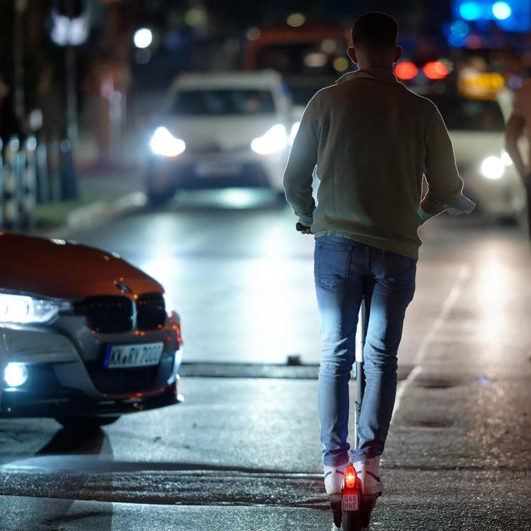 Menschen auf E-Scootern fahren in der Nacht durch eine Straße in der Düsseldorfer Altstadt. Auch Autos sind auf der Straße unterwegs.