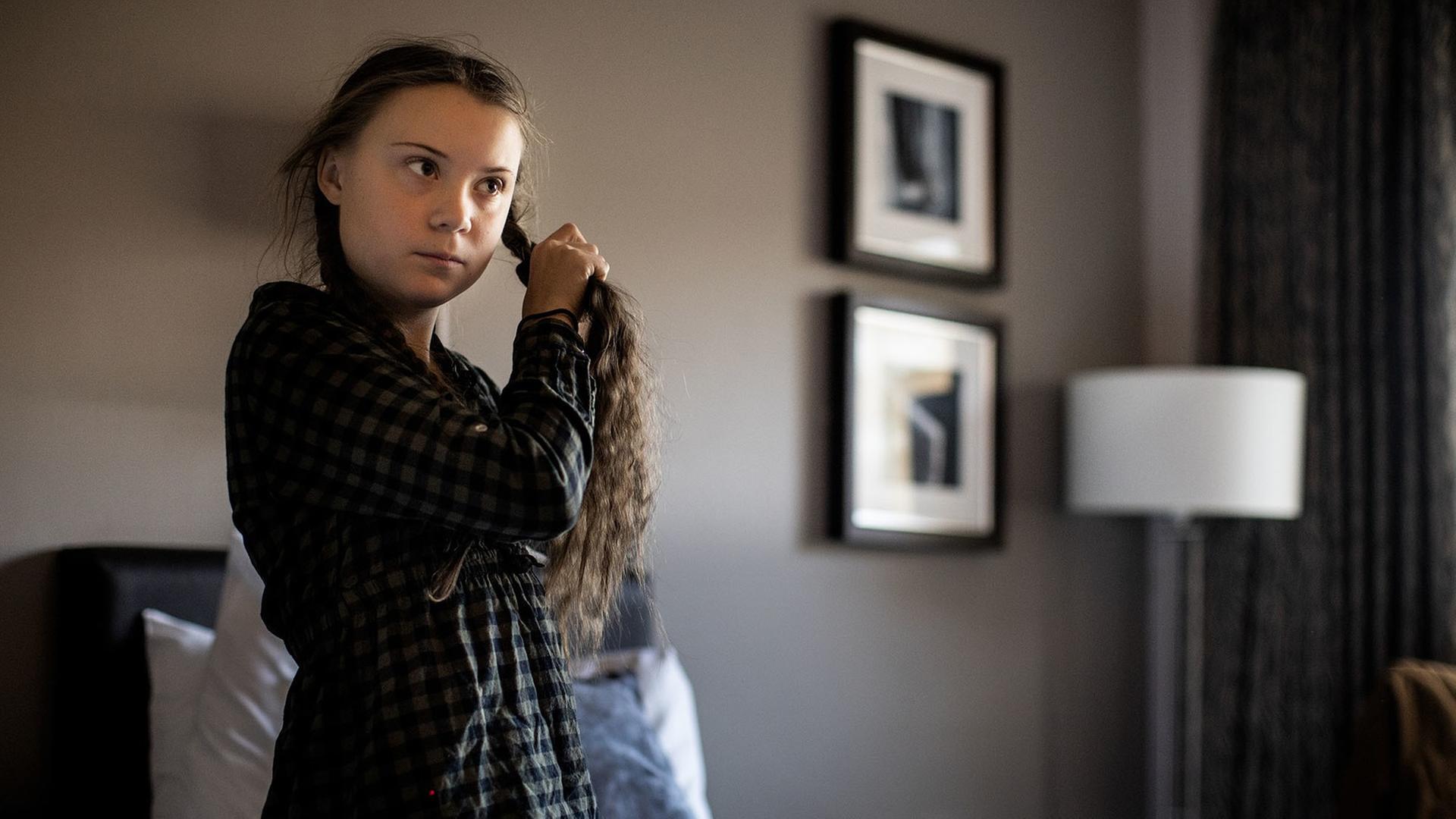 Das Foto zeigt die Klimaaktivistin Greta Thunberg, wie sie in einem Hotelzimmer einen Zopf bindet.