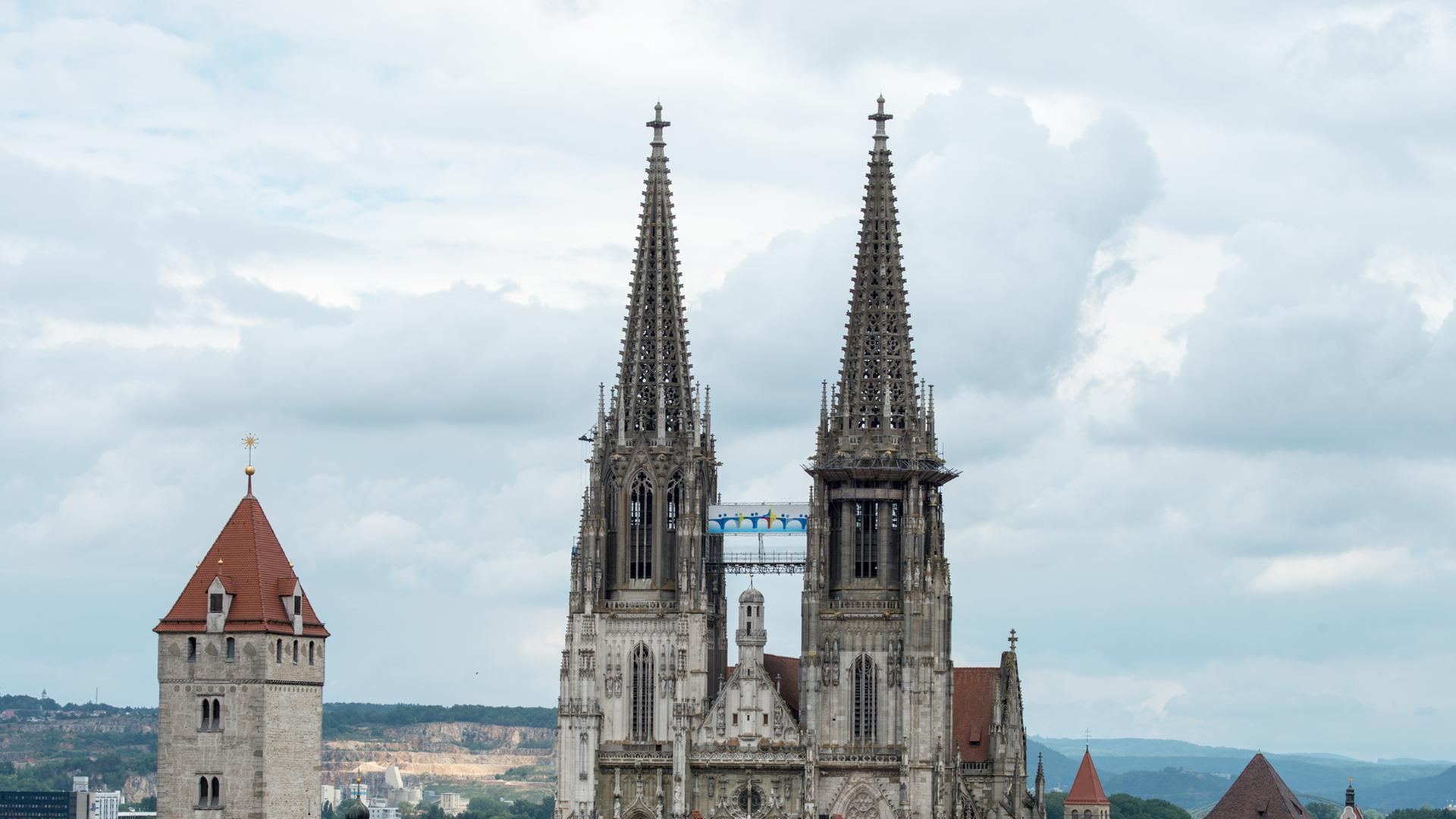 Ein Plakat mit dem Logo des Katholikentages hängt zwischen den Türmen des Doms St. Peter in Regensburg.