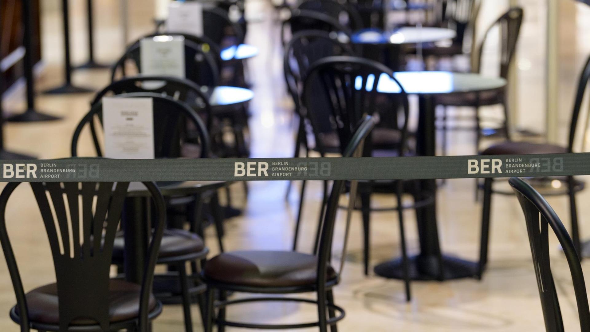 Ein wegen der Corona-Regeln aufgebautes Absperrband mit dem Logo BER verhindert, dass sich Reisende an die Tische eines Cafes im Duty-Free-Bereich des Terminal 1 setzen können.