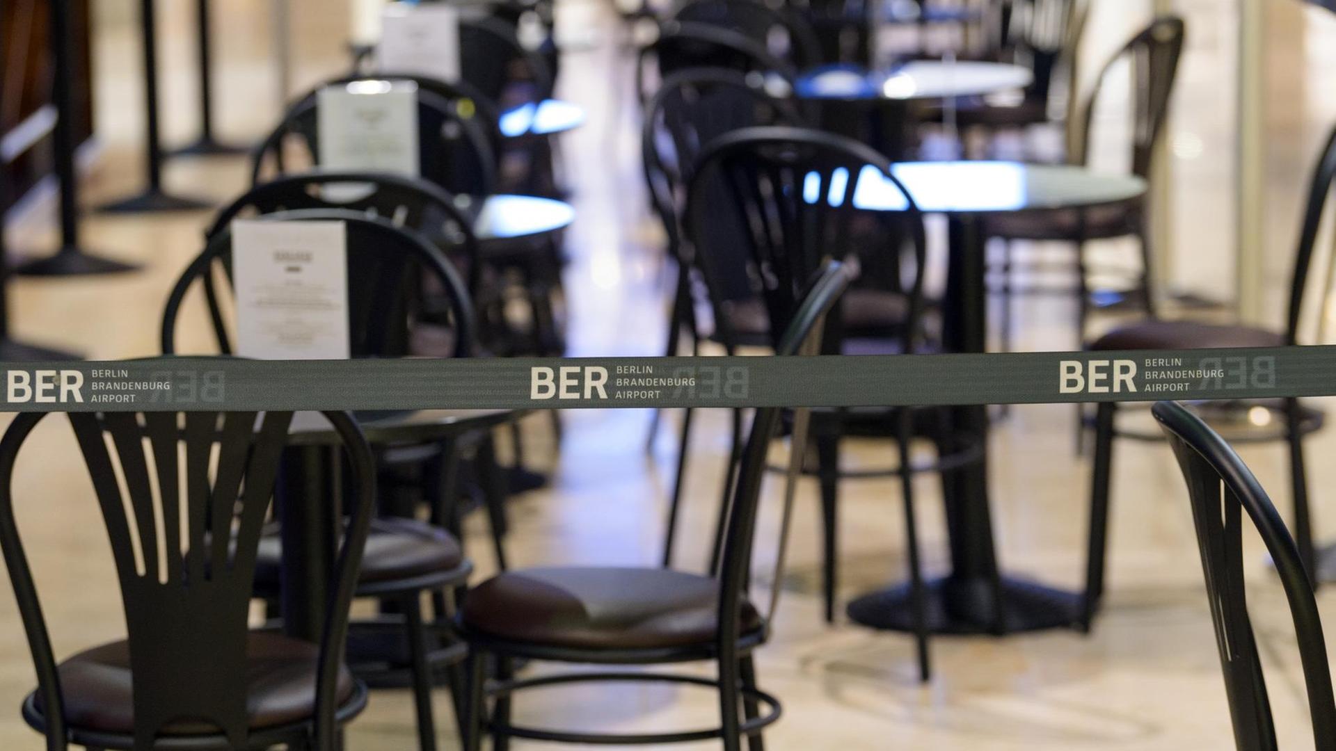 Ein wegen der Corona-Regeln aufgebautes Absperrband mit dem Logo BER verhindert, dass sich Reisende an die Tische eines Cafes im Duty-Free-Bereich des Terminal 1 setzen können. Ein wegen der Corona-Regeln aufgebautes Absperrband mit dem Logo BER verhindert, dass sich Reisende an die Tische eines Cafes im Duty-Free-Bereich des Terminal 1 setzen können.