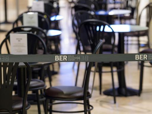 Ein wegen der Corona-Regeln aufgebautes Absperrband mit dem Logo BER verhindert, dass sich Reisende an die Tische eines Cafes im Duty-Free-Bereich des Terminal 1 setzen können.