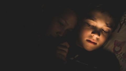 Zwei Kinder liegen im Bett, das Licht ist schon erloschen und sie sehen müde aus.