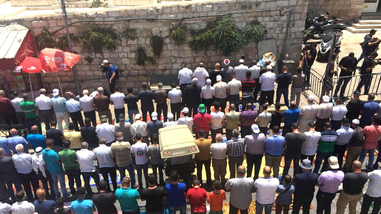Hunderte Muslime knien in langen Reihen mitten auf einer Straße vor der Altstadt Jerusalems und beten.