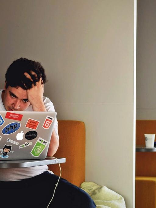 Ein junger Mann sitzt vor einem Laptop und rauft sich die Haare.