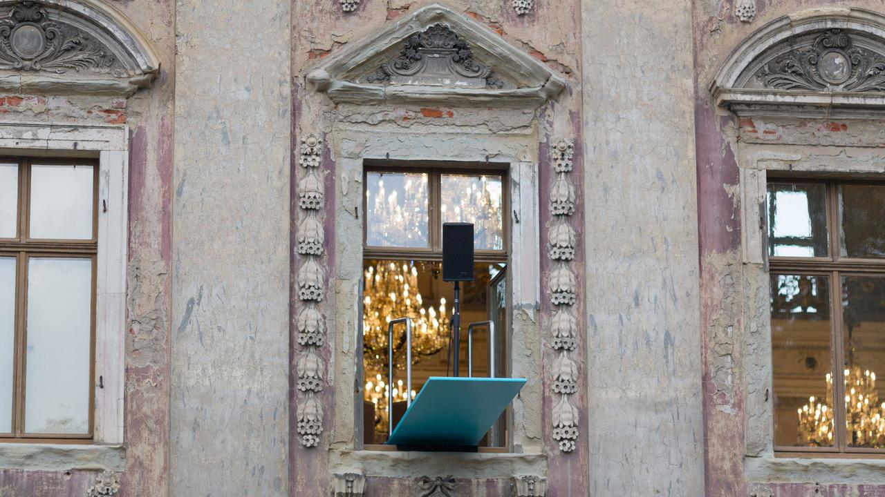 Ein geöffnetes Fenster mit einem daraus ragendem Brett mit einer Box darauf. Im Hintergrund sind einige Kronleuchter zu sehen Ein geöffnetes Fenster mit einem daraus ragendem Brett mit einer Box darauf. Im Hintergrund sind einige Kronleuchter zu sehen