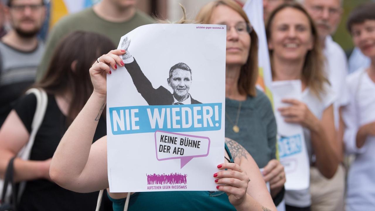 09.08.2019, Sachsen, Grimma: Die Teilnehmerin einer Gegendemonstration hält auf dem Marktplatz ein Transparent mit der Aufschrift "Nie wieder". 
