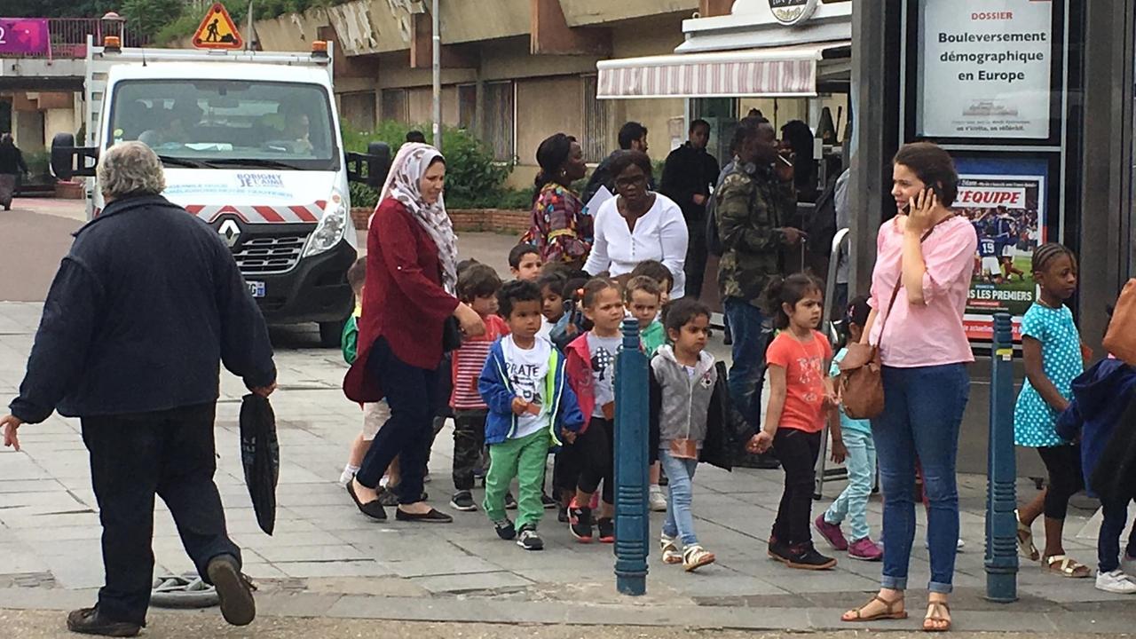 Schulkinder werden von ihren erwachsenen Begleitern durch die Straßen gelotst - eine der Mütter trägt ein Kopftuch