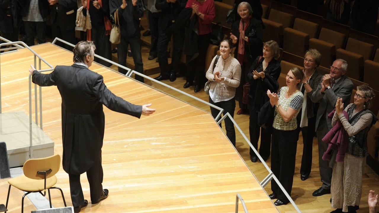 Der Dirigent Mariss Jansons steht ausgebreiteten Armen auf der Bühne, ganz nah an ihm zujubelnden Menschen am Bühnenrand. Der Dirigent Mariss Jansons steht ausgebreiteten Armen auf der Bühne, ganz nah an ihm zujubelnden Menschen am Bühnenrand.