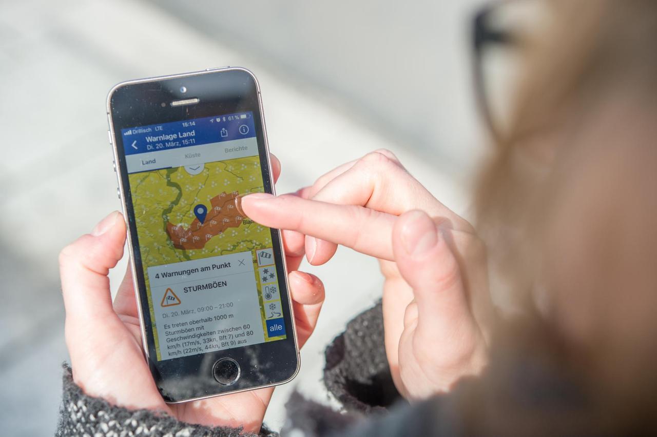 ILLUSTRATION - Eine Frau haelt am 21.03.2018 in Berlin ein Smartphone in der Hand, das eine Unwetter-Warnungs-App zeigt (gestellte Szene). Foto: Robert Guenther