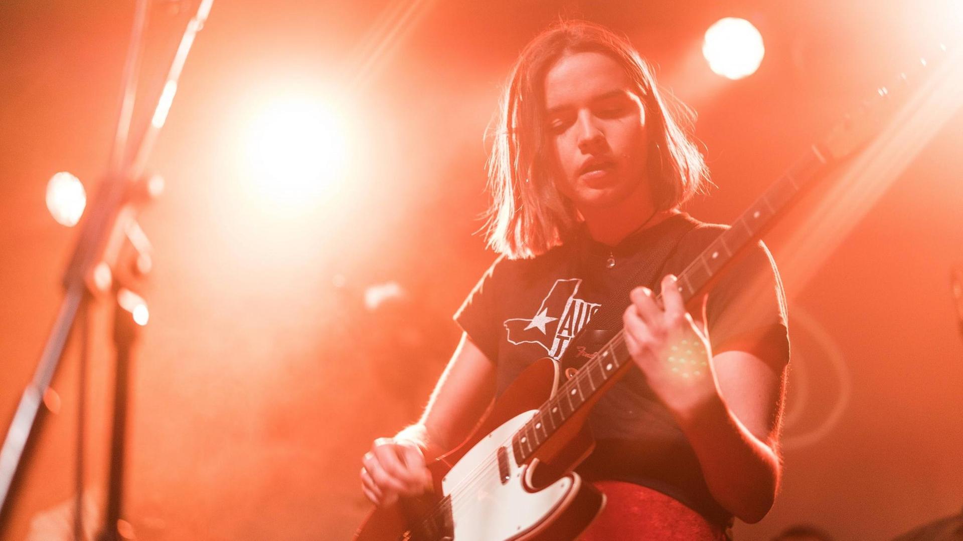 Die Sängerin schaut auf ihre E-Gitarre und ist in rotes Licht getaucht. Die Sängerin schaut auf ihre E-Gitarre und ist in rotes Licht getaucht.