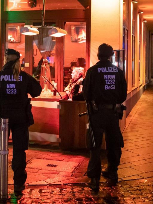 Das Bild zeigt Polizisten, die ein Lokal bei Nacht von außen umstellt haben.