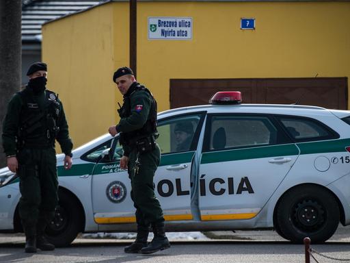 Zwei Polizisten und ein Polizeiauto stehen vor einem gelben Haus.