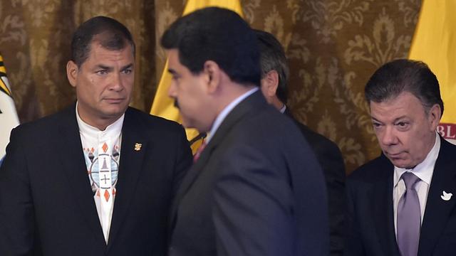 Correa und Santos stehen vor einer braunen Wand mit gelben Fahnen. Maduro geht im Vordergrund an ihnen vorbei.
