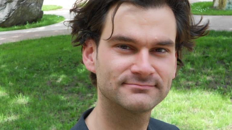 Porträt des Philosophen Raphael Rauh, im dunklen Sakko, in einem begrünten Innenhof Porträt des Philosophen Raphael Rauh, im dunklen Sakko, in einem begrünten Innenhof