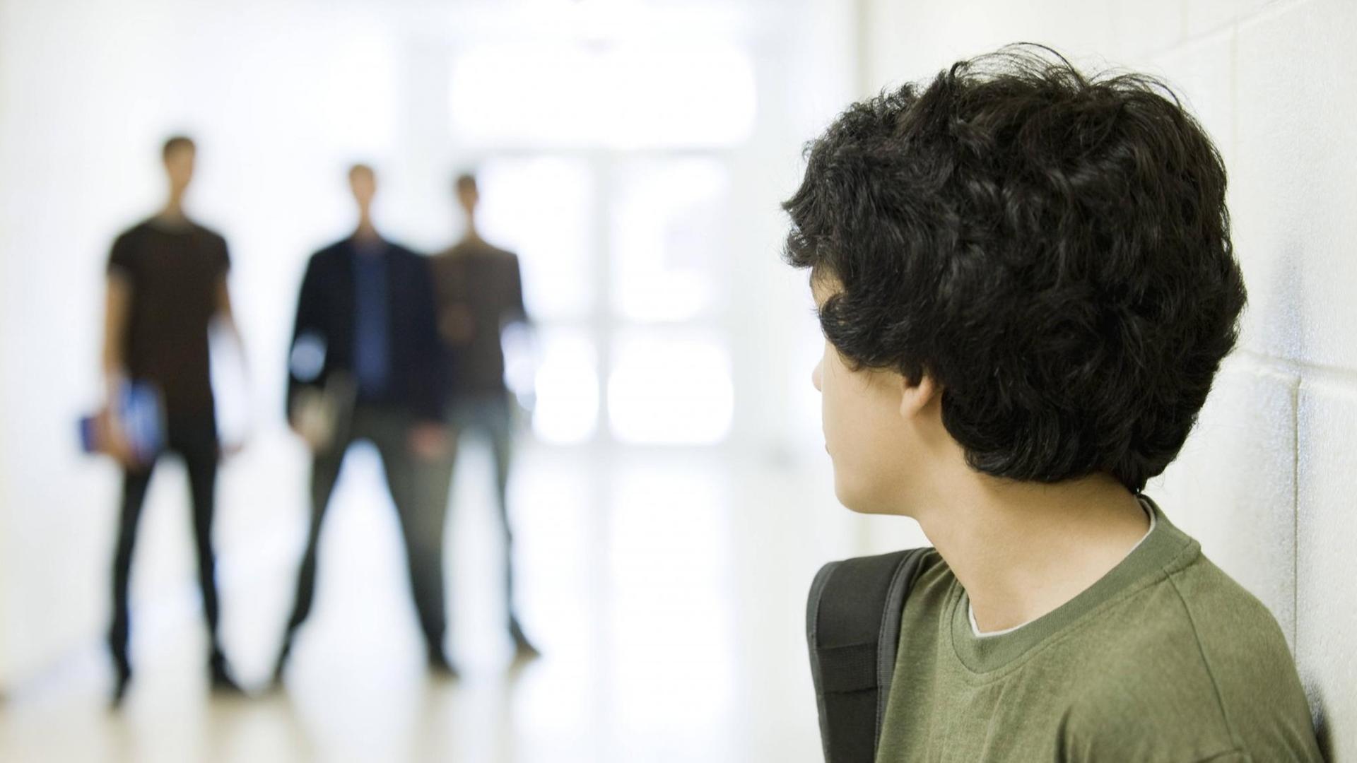 Ein junger Teenager blickt über die Schulter. Im Hintergrund sind die unschargen Silouetten von drei größeren Schülern zu erkennen. Ein junger Teenager blickt über die Schulter. Im Hintergrund sind die unschargen Silouetten von drei größeren Schülern zu erkennen.
